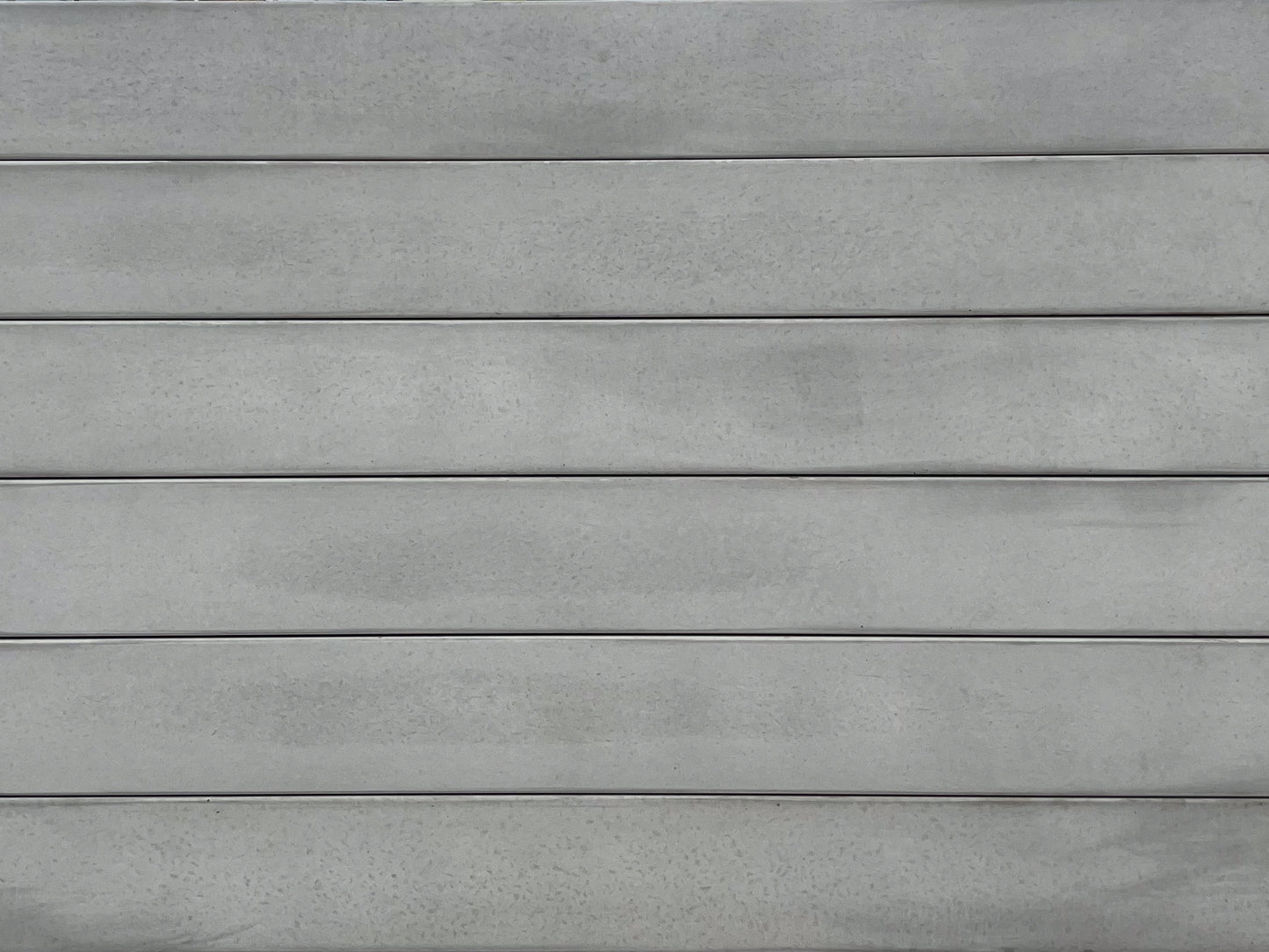 Close-up of the Smooth Plain Grey 2 bar Concrete Sleeper by 0, featuring a gray metal-like surface with horizontal, evenly spaced ridges and subtle color variations for a modern, matte look.